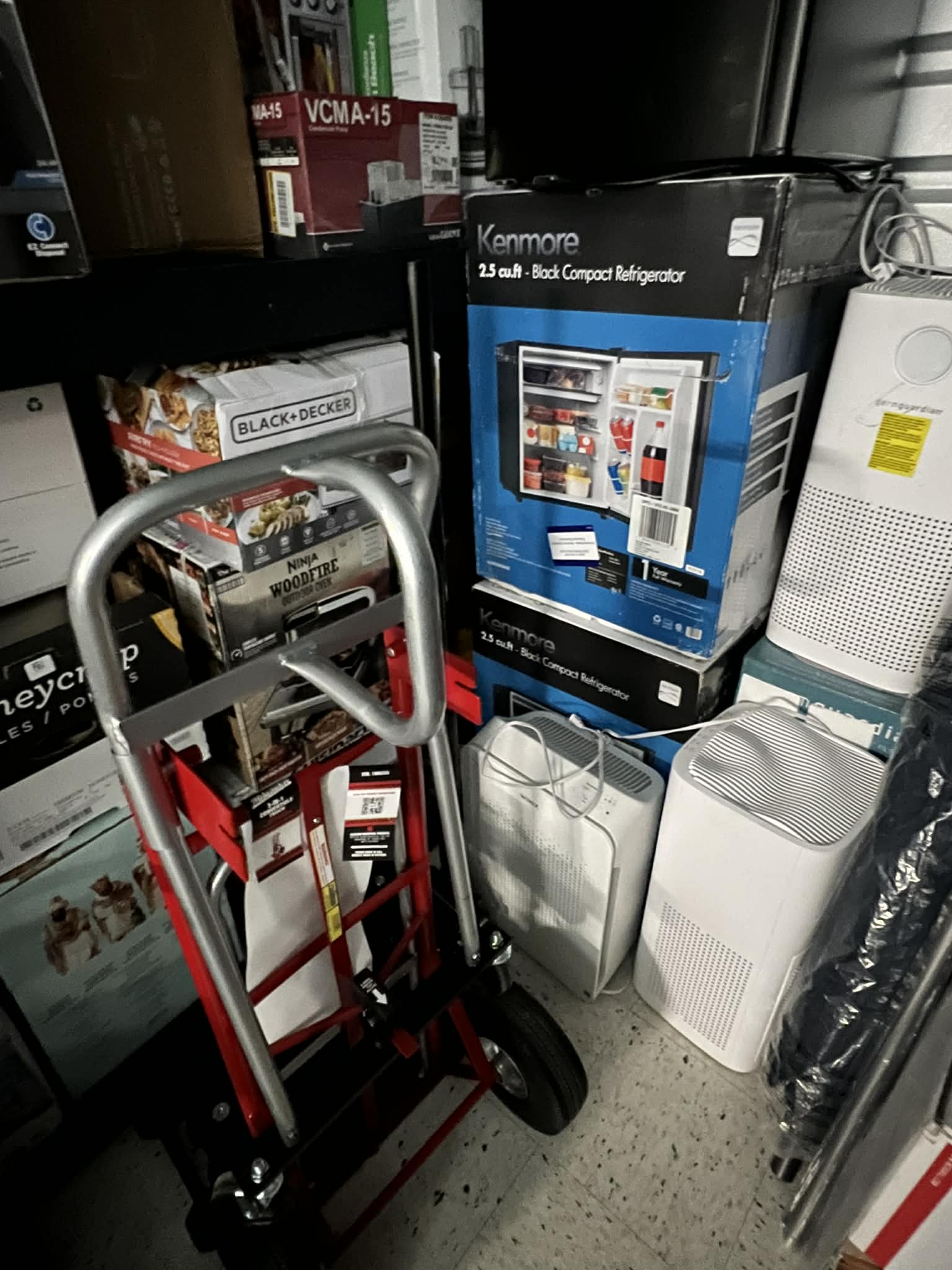 Compact refrigerators, air purifiers, and a hand truck staged in the warehouse